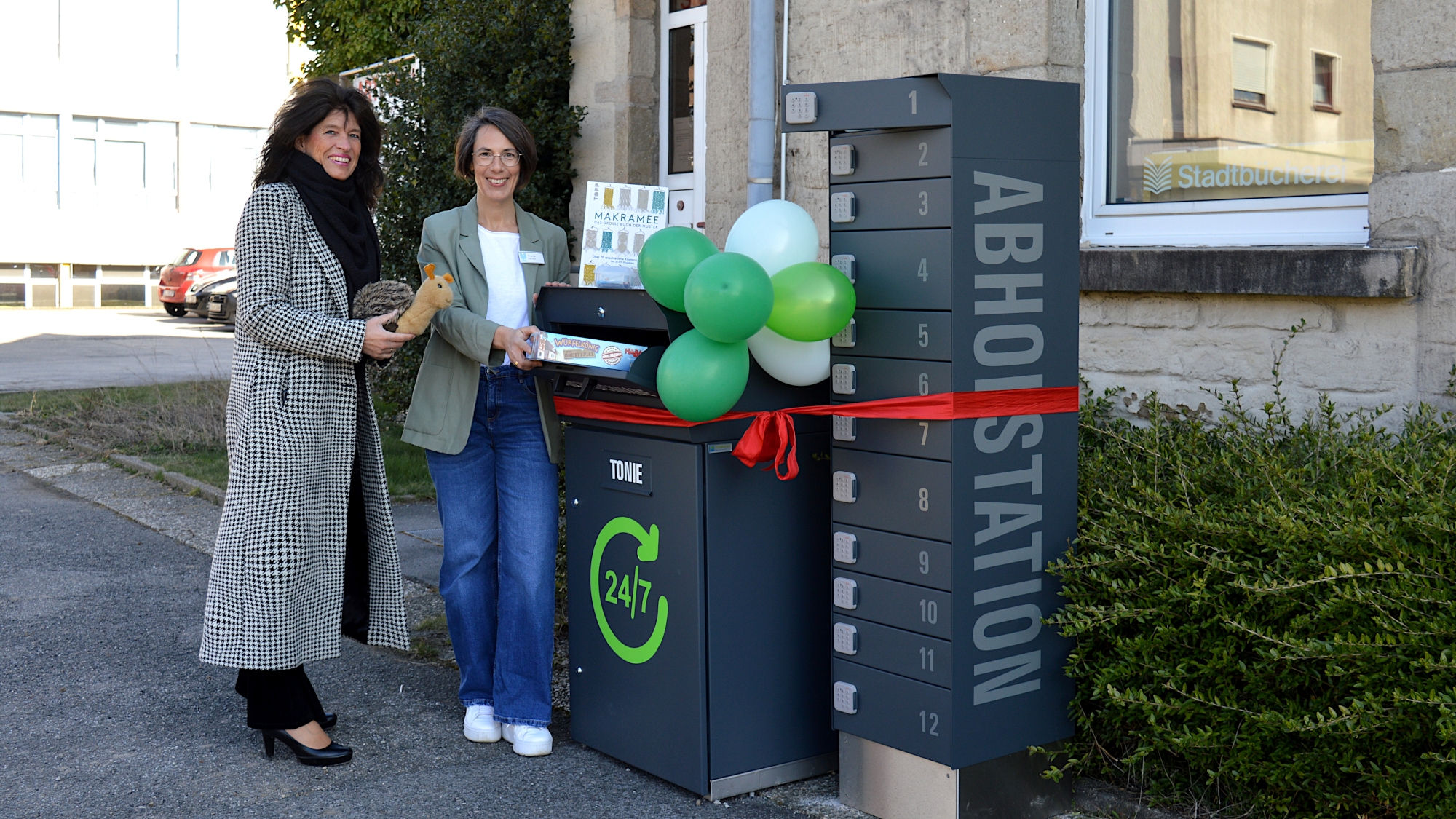 Sabine Noll und Ricarda Gärtner stellen gemeinsam mit Schnecke Tilly, dem Büchereimaskottchen, die neue Abholstation und die neue Rückgabebox vor.