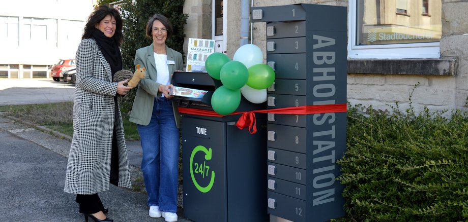 Sabine Noll und Ricarda Gärtner stellen gemeinsam mit Schnecke Tilly, dem Büchereimaskottchen, die neue Abholstation und die neue Rückgabebox vor.