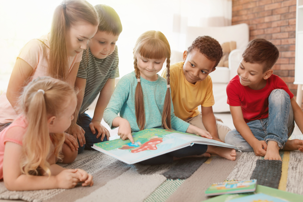 Niedliche kleine Kinder sitzen auf dem Boden und lesen gemeinsam im Haus Buch