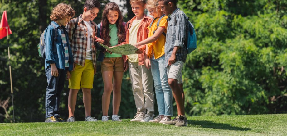 fröhliche Gruppe multikultureller Kinder schaut auf Landkarte in der Nähe von Bäumen im Park