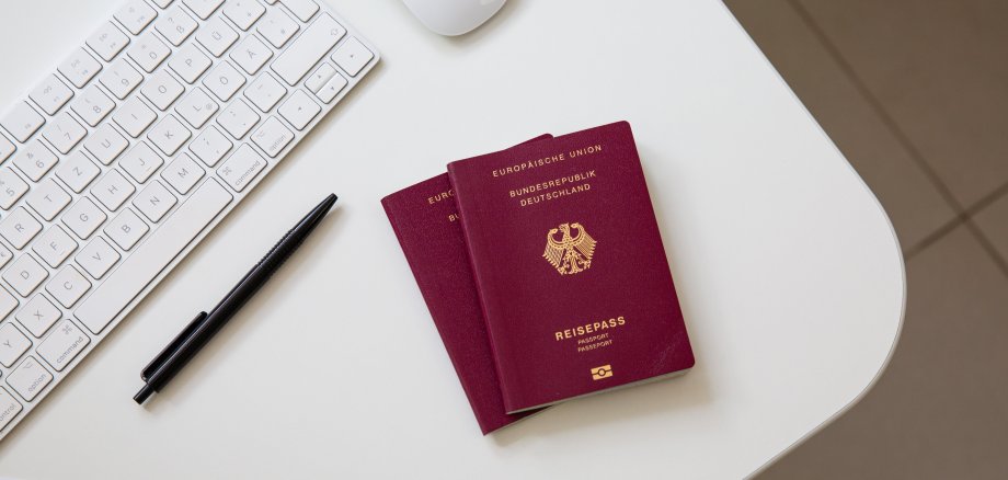 Draufsicht auf einen deutschen Pass auf weißem Tisch, mit schwarzer Pfanne, Computertastatur und Maus.